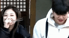 a man and a woman are sitting next to each other and the woman is eating with chopsticks .