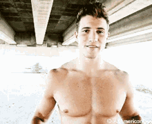 a shirtless man is standing under a bridge looking at the camera .