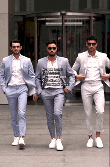 three men wearing suits and sunglasses are standing in front of a building