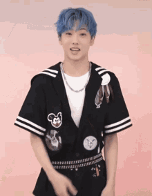 a young man with blue hair is wearing a black jacket with a white t-shirt and a necklace .