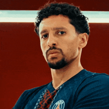 a man with curly hair and a beard is wearing a blue shirt with the letters psg on it