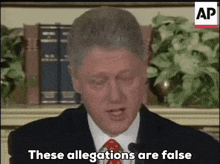 a man in a suit and tie is speaking into a microphone and says " these allegations are false "