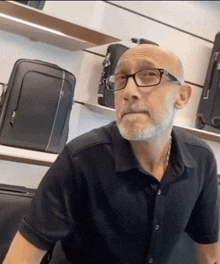 a bald man with glasses and a beard is sitting in front of a display of suitcases
