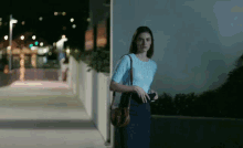 a woman in a blue sweater and blue skirt is walking down a sidewalk at night