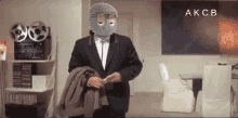 a man in a suit has a mask on his face and the word akcb is on the bottom right