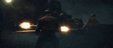 a man is holding a gun in a dark room with a lot of fire coming out of it .
