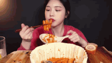 a woman is eating a bowl of food with chopsticks and a spoon