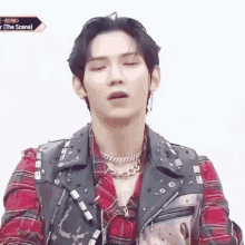 a young man wearing a plaid shirt and a leather vest