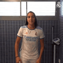 a woman in an emirates fly better shirt stands in front of a tiled wall