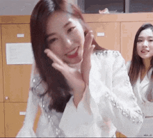 two women are standing next to each other in a room . one of the women is smiling and making a peace sign .