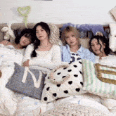 four women are laying on a bed with pillows and one has the letter n on it