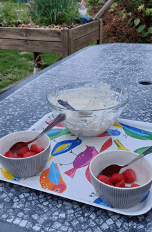 two bowls of strawberries sit on a colorful tray with birds on it