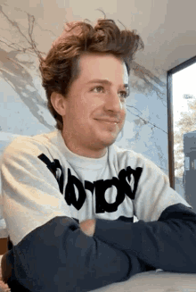 a young man wearing a sweater that says ' nothing ' on it is sitting at a table with his arms crossed