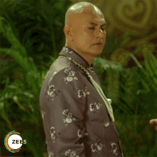 a man wearing a floral jacket and pearls is standing in front of a sign that says zees