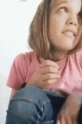 a young girl wearing a pink shirt and jeans is looking up