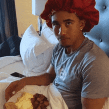 a man wearing a red hat sits on a bed with a plate of food in front of him
