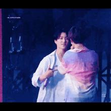 two men are hugging each other on a stage and one is wearing a colorful shirt .