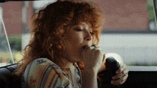 a woman with red curly hair is smoking a cigarette
