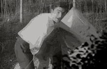 a man is kneeling down in front of a tent in a field .