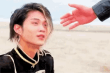 a man is reaching out towards another man 's hand on a beach .