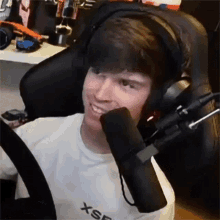 a man wearing headphones and a microphone is smiling while sitting in a chair .