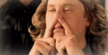 a man with long hair is making a funny face with his fingers in his nose .