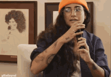 a woman wearing glasses and an orange hat is holding a microphone in front of a framed picture of a woman