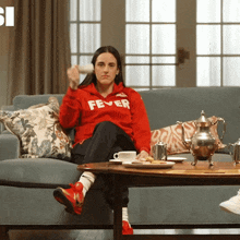 a woman is sitting on a couch wearing a red fever sweatshirt