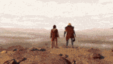 two people standing on top of a rocky hill looking out over a desert landscape