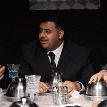 a man in a suit and tie is sitting at a table with silverware