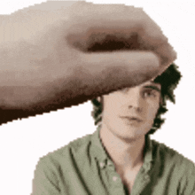 a hand is touching a man 's forehead with a green shirt on