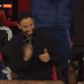 a man with a beard is smiling in front of a scoreboard with the number 7 on it
