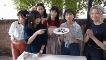 a group of young women are standing around a table with a plate of food in front of them