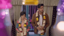 a man and a woman standing next to each other wearing garlands of flowers