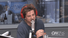 a man wearing red headphones stands in front of a microphone in a onair studio