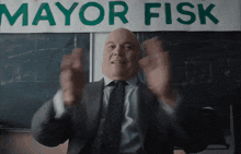 a bald man in a suit and tie is standing in front of a sign that says mayor fisk