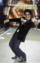 a man in a tuxedo is singing into a microphone in front of a sign that says " victoria "