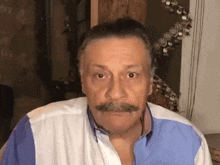 a man with a mustache and a blue and white shirt is making a funny face .