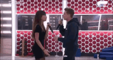 a man and a woman singing into microphones in front of a red polka dot wall .