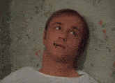 a man with a cigarette in his mouth leaning against a wall with flowers on it