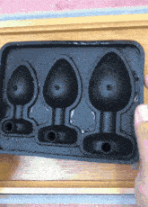 a person is holding a black ice cube tray with three different sizes of ice cubes