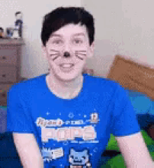 a young man wearing a blue t-shirt with a cat face paint on his face .