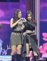 two women are making a heart with their hands on a stage .