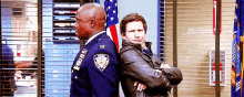 two police officers are standing back to back with their arms crossed .