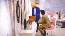 a man in a blue suit and turban is standing next to another man in a living room .