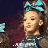 a cheerleader with a blue bow on her head is making a funny face and says julie ? hmm .