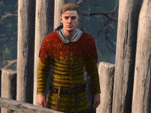 a man in a yellow and red sweater is standing next to a fence