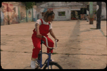 a woman in red overalls is riding a bike in front of a building that has peace written on it