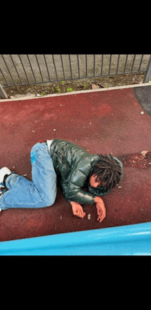 a person laying on the ground wearing a green jacket and jeans