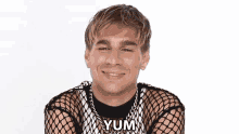 a man wearing a fishnet top is smiling and says yum
